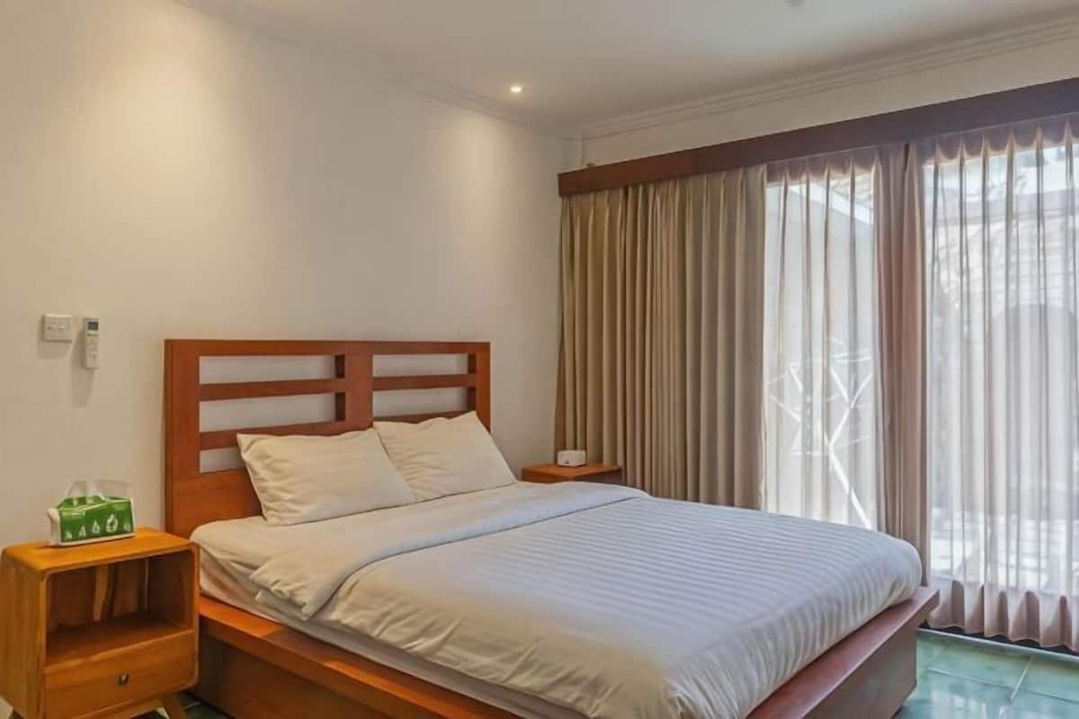 Una habitación de hotel con una cama de madera, una mesita de noche, una caja verde y una ventana con cortinas.
