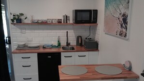 A compact kitchen with white cabinets, a microwave, a toaster, and a sink. There are two stools and a small table with two round mats.