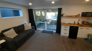 A compact living space with a sofa, kitchenette, and a sliding glass door leading to an outdoor area.