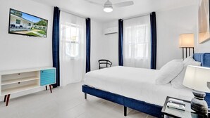 A modern hotel room with a large bed, a desk with a chair, a TV mounted on the wall, and a ceiling fan.