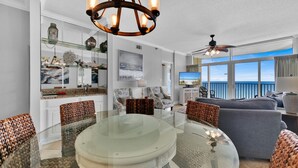 Una sala moderna con una mesa de comedor de cristal, sillas de mimbre, un sofá gris y un balcón con vistas al océano.