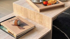 Een moderne woonkamer met een houten bijzettafeltje, een glazen theepot, twee kopjes en een dienblad met lekkernijen.
