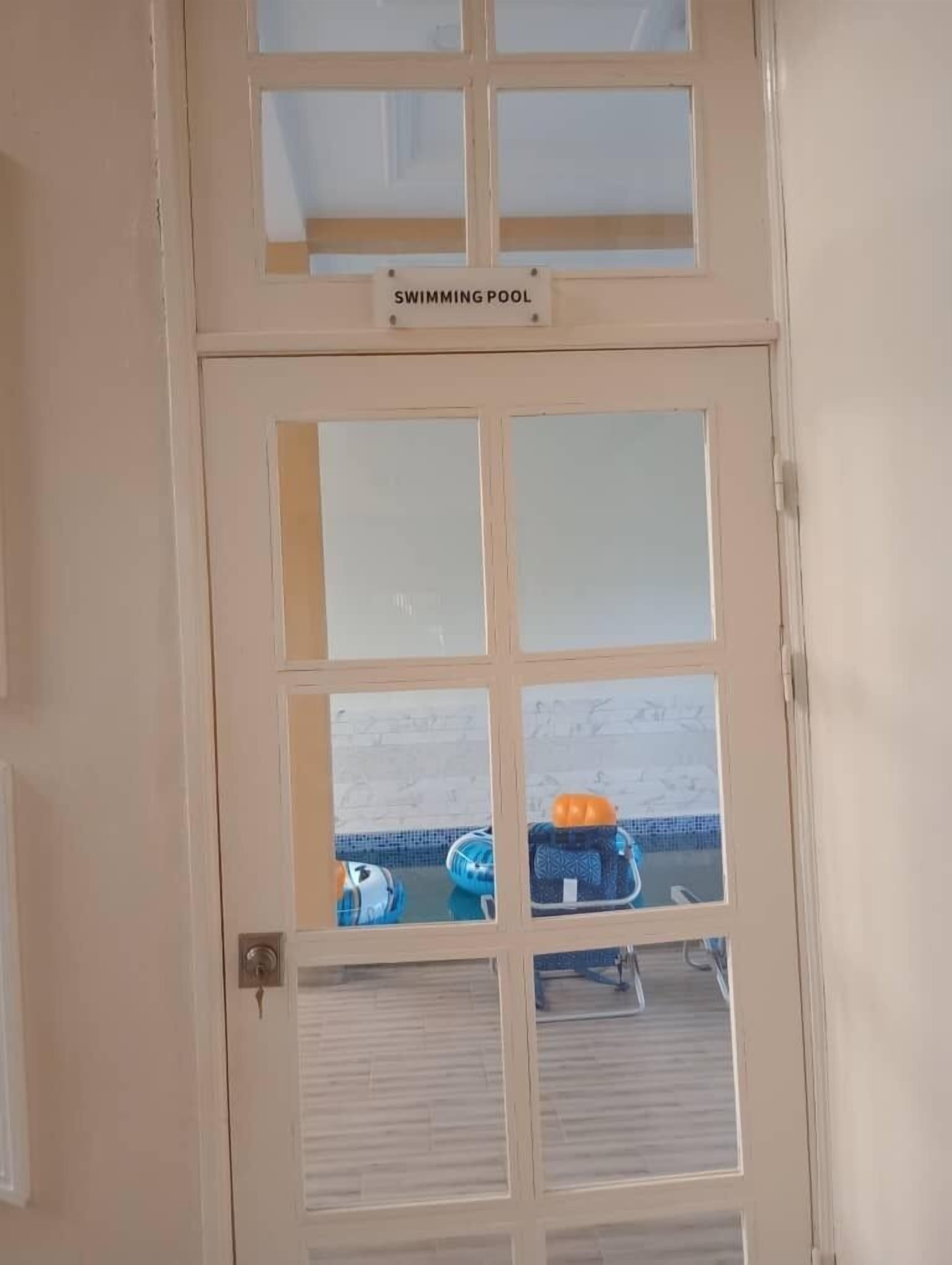 Puerta con un letrero que dice "SWIMMING POOL" y vista de muebles junto a la piscina.