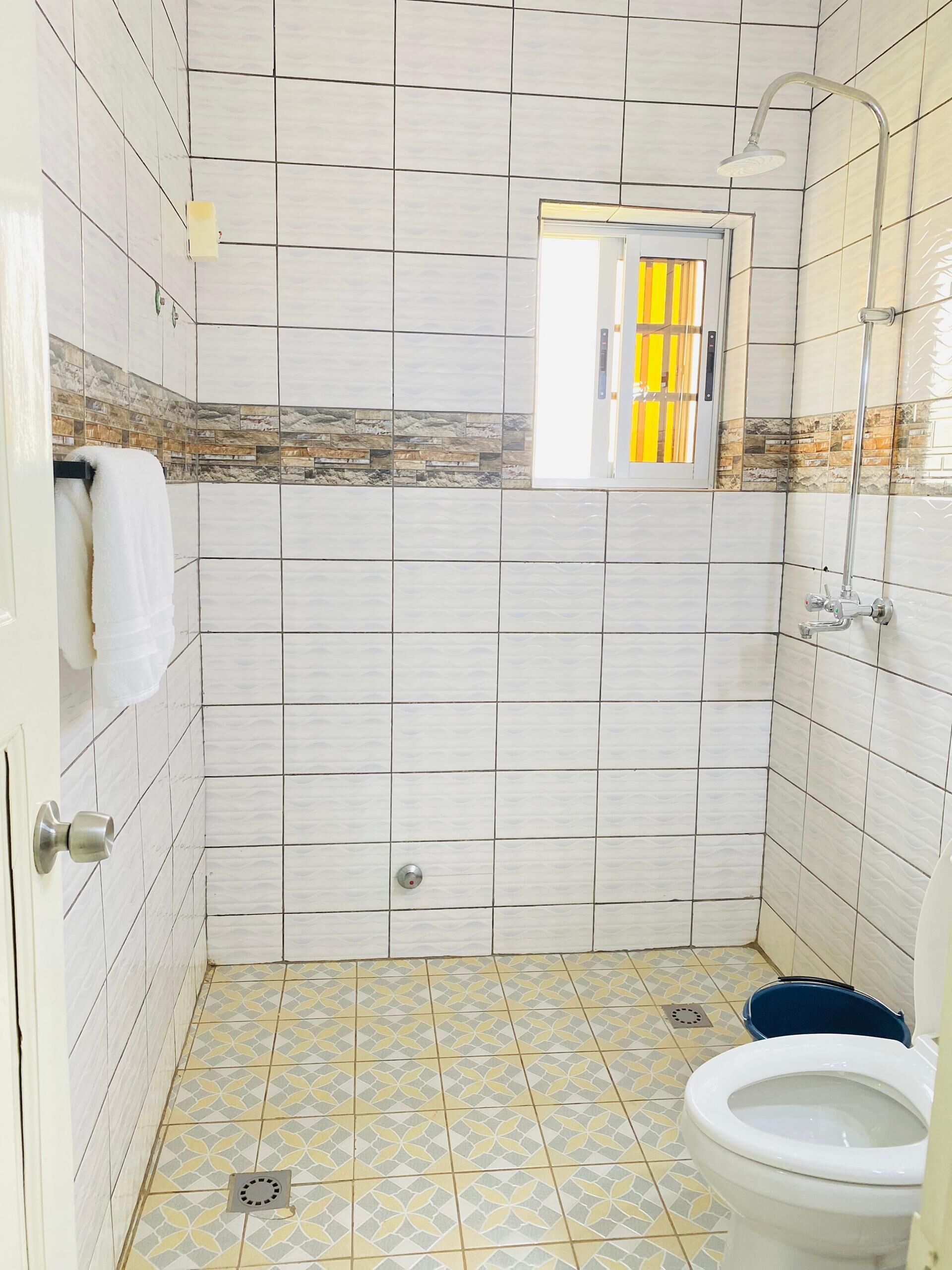 Een badkamer met witte betegelde wanden, een douche, een toilet en een raam met gele zonwering.