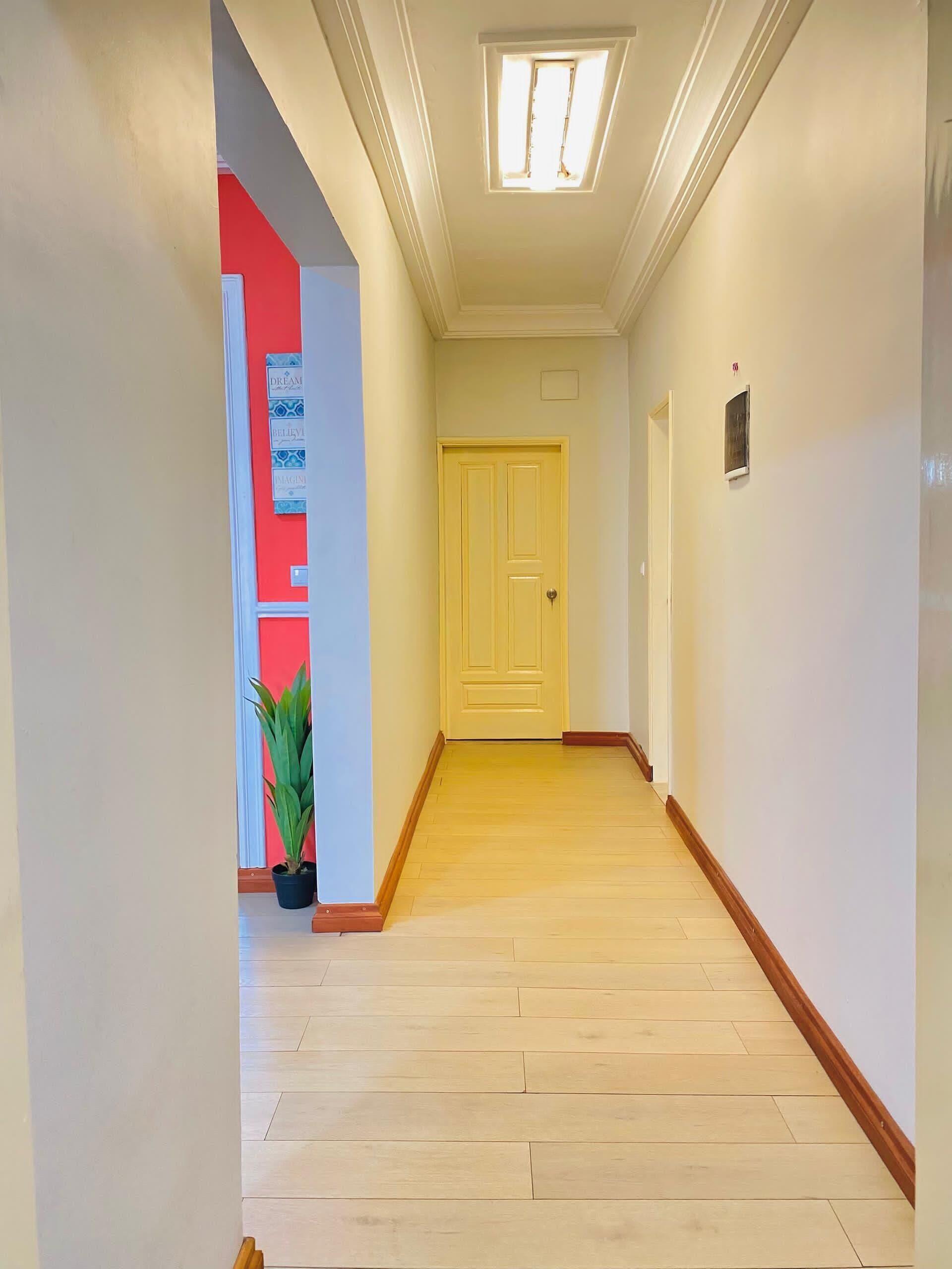 A hallway with a wooden floor, a yellow door, and a small plant.