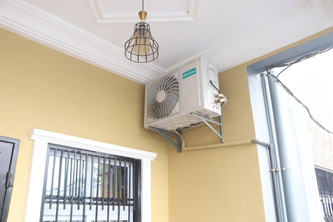 A corner room with a white ceiling, a window with black bars, and an air conditioning unit mounted on the wall.