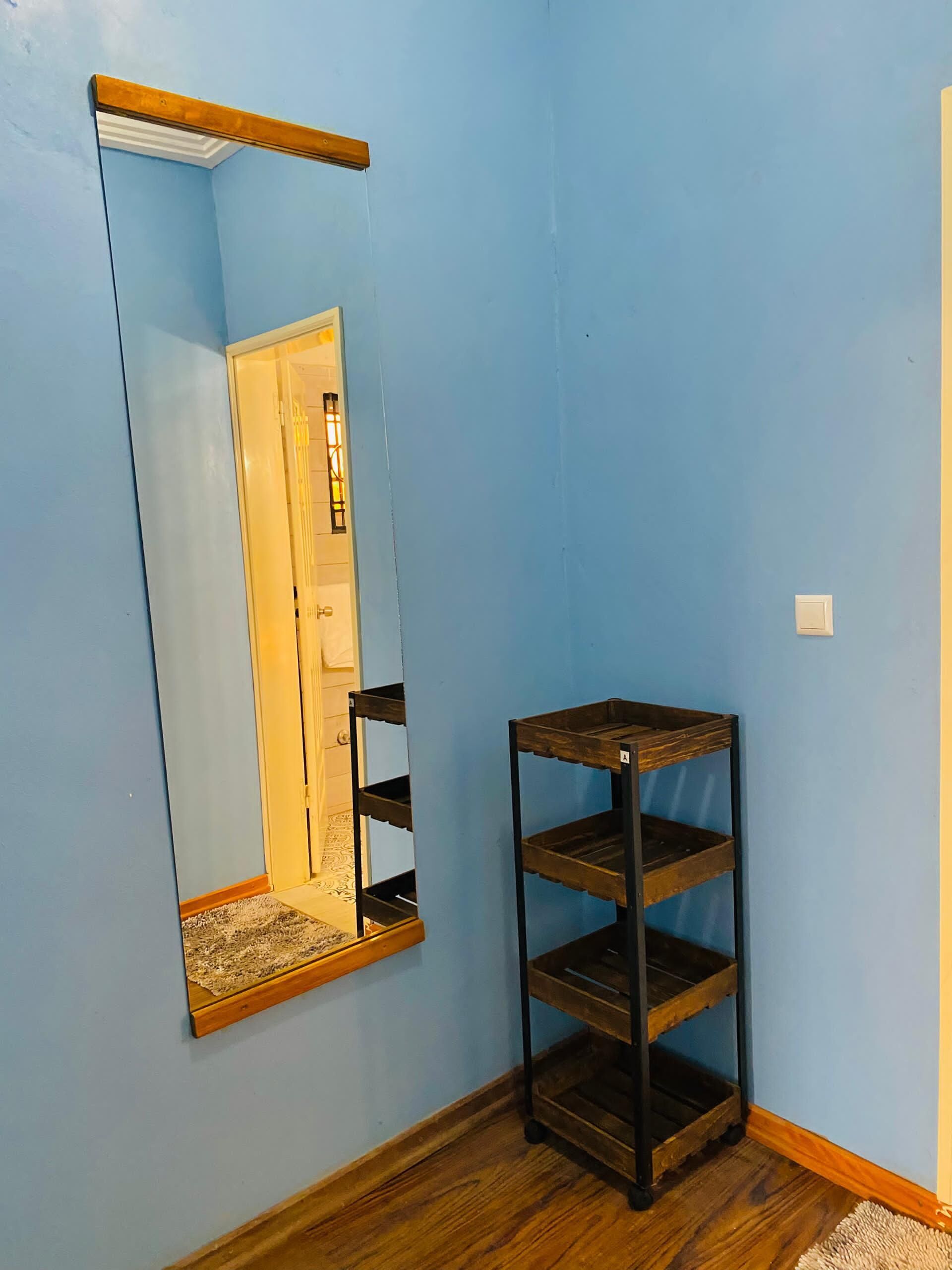 A room with a blue wall, a wooden floor, a mirror with a wooden frame, and a black metal shelf unit.