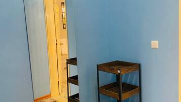 A room with a blue wall, a wooden floor, a mirror with a wooden frame, and a black metal shelf unit.