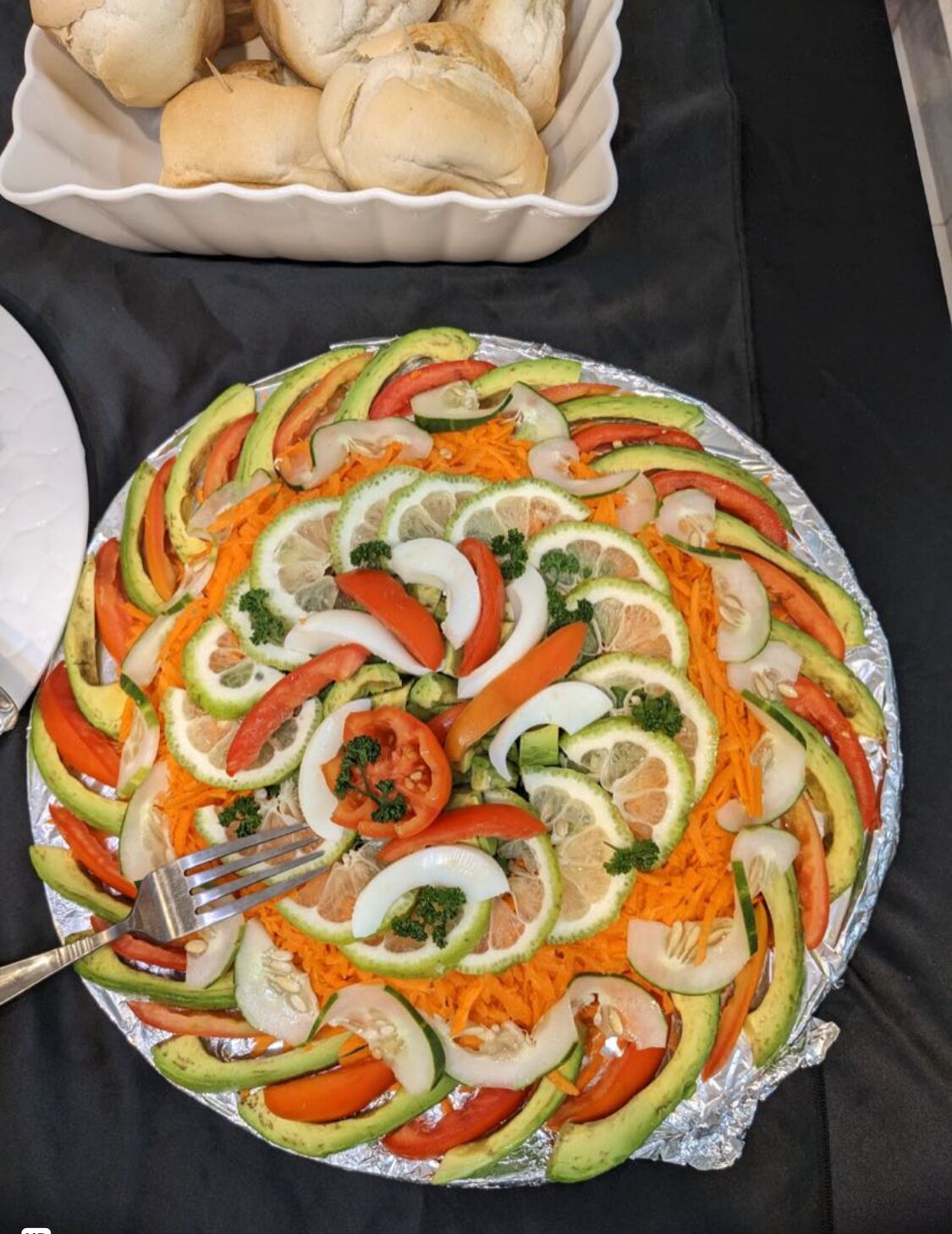 Una bandeja con vegetales cortados y panecillos sobre una mesa.
