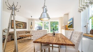 Et spiseområde med et træbord, hvide polstrede stole og en hængende lampe.