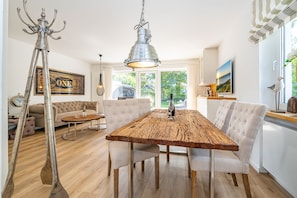 A dining area with a wooden table, white upholstered chairs, and a hanging light fixture.
