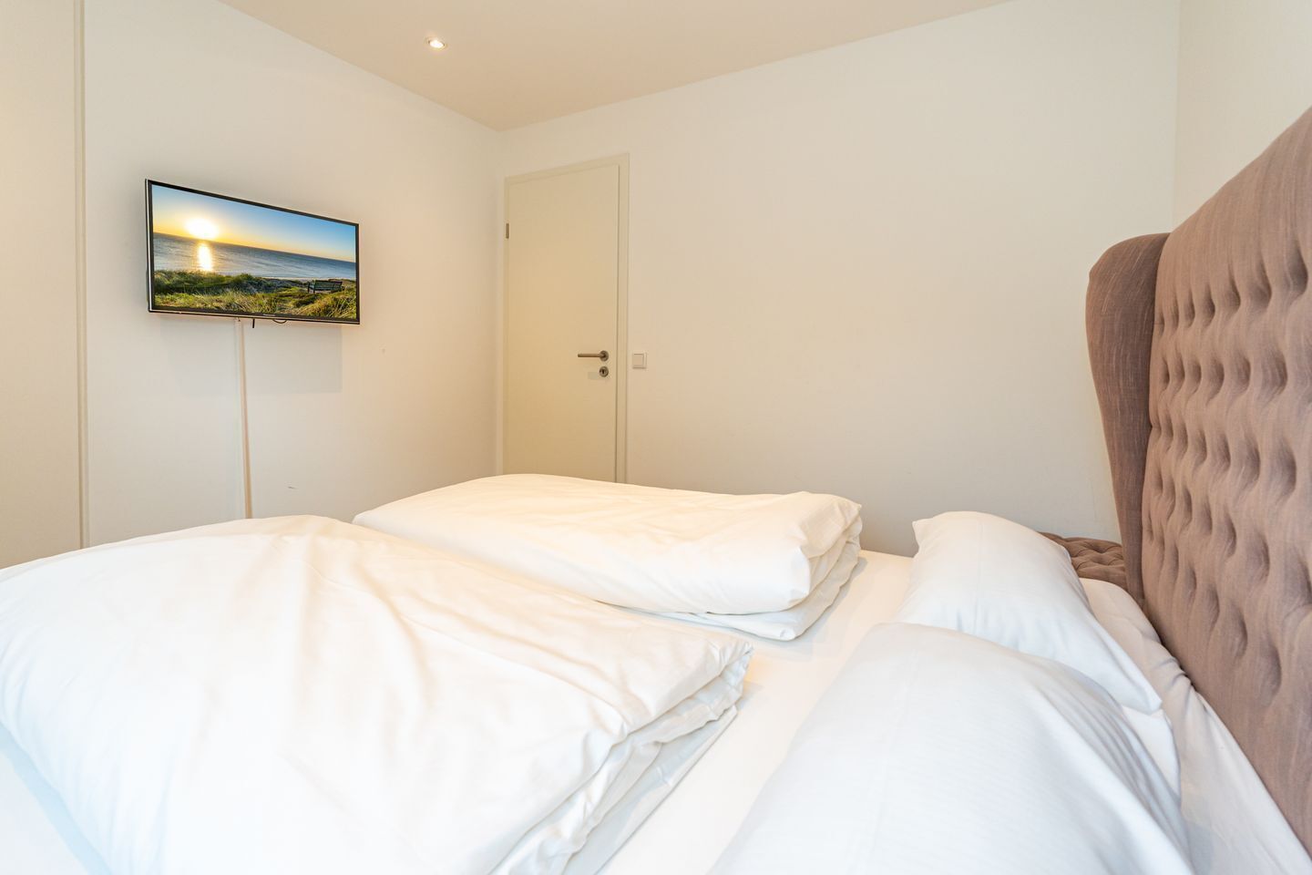 A bedroom with a bed, a television mounted on the wall, and a door.