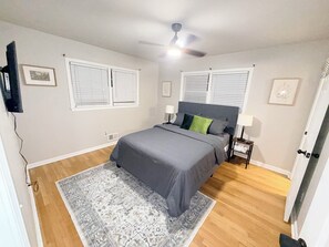 Una camera da letto con un letto, due comodini, una ventola a soffitto e una finestra con persiane.