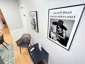 A room with a framed newspaper on the wall, a small table with a remote control, and two chairs.