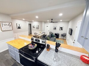 A modern kitchen with a central island, a dining area with a table and chairs, and a living room with a sofa and a television.