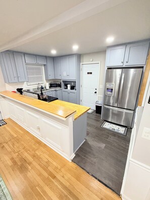 A modern kitchen with grey cabinets, a stainless steel refrigerator, and a wooden countertop.