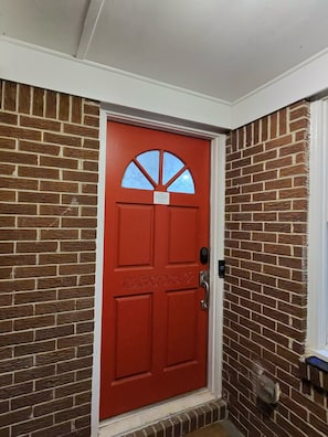 A red door with a sign, a brick wall, and a window with a flower design.