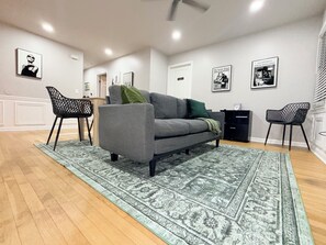 Un soggiorno con un divano grigio, un tappeto decorato e sedie nere.