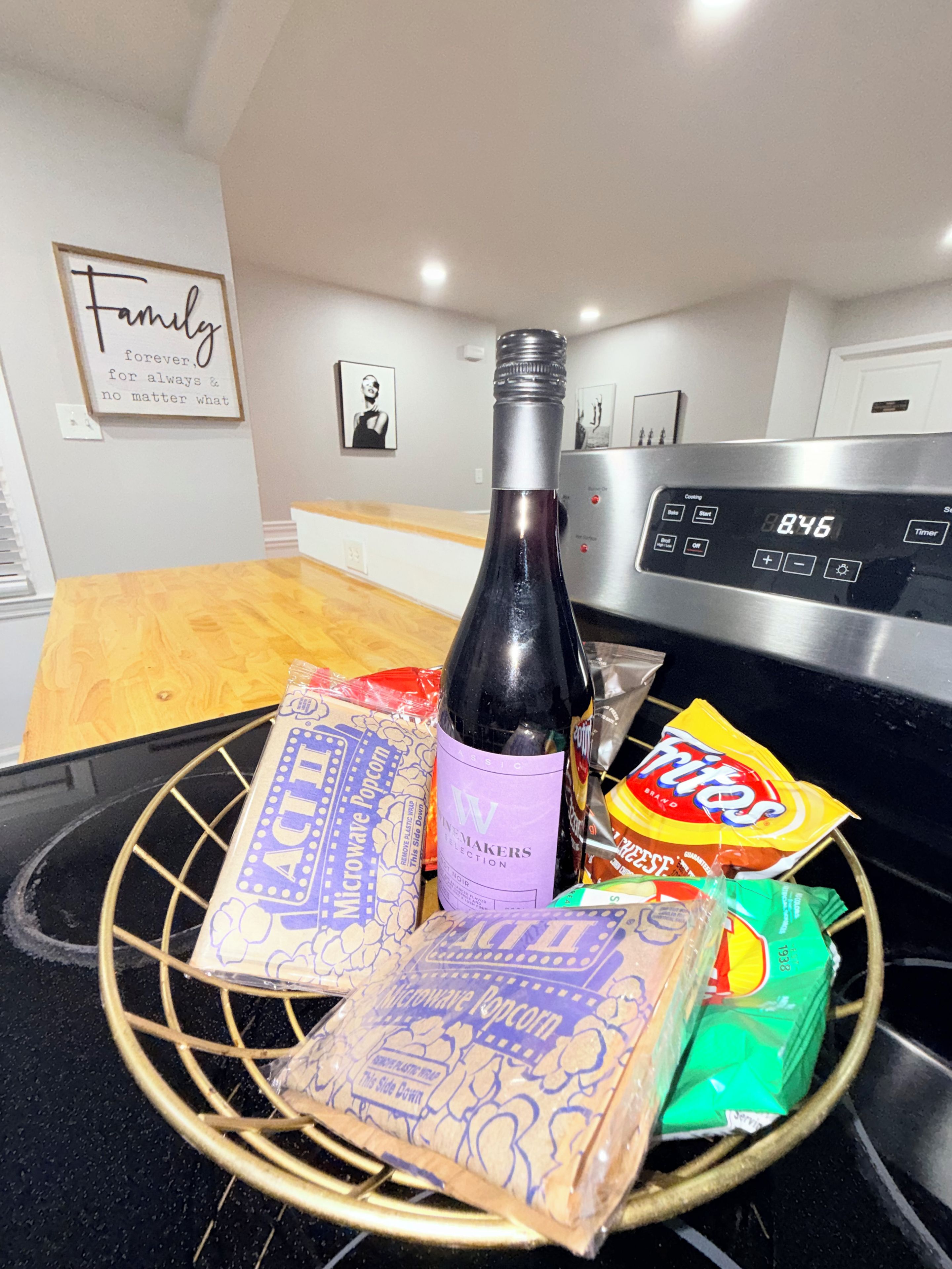 A kitchen counter with a microwave popcorn bag, a bottle of wine, a bag of popcorn, and a bag of chips.