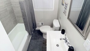 A bathroom with a bathtub, toilet, sink, and a shower curtain. - Cozy 3BR Retreat • Near ATL Airport & Downtown (Conley)
