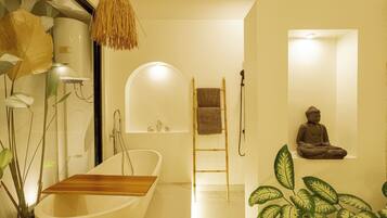 A modern bathroom with a freestanding bathtub, a towel rack, a small shelf, and a Buddha statue.