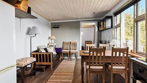 Un salon chaleureux avec un plancher en bois, un canapé, une table à manger avec des chaises et une grande fenêtre laissant entrer la lumière naturelle.