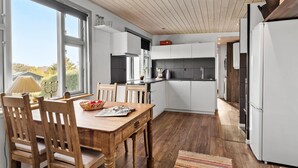 Une cuisine moderne avec des meubles blancs, une table à manger en bois et une vue sur l’extérieur.