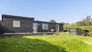Un bâtiment moderne, de couleur sombre, doté de nombreuses fenêtres et d’un petit jardin à l’avant.