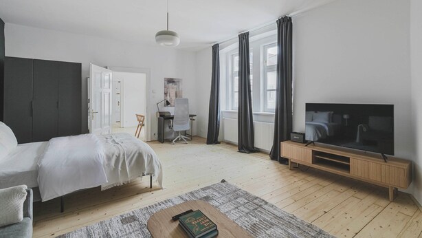 A modern bedroom with a bed, a desk, a TV, and a bookshelf. - Nice Landstraße Studio w/ Washer & Balcony, by Blueground (Vienna)
