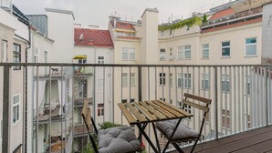 A balcony with a wooden table and chairs, a metal railing, and a view of adjacent buildings. - Nice Landstraße Studio w/ Washer & Balcony, by Blueground (Vienna)