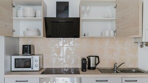 A modern kitchen with white cabinets, a black range hood, a microwave, a coffee maker, and a sink. - Nice Landstraße Studio w/ Washer & Balcony, by Blueground (Vienna)