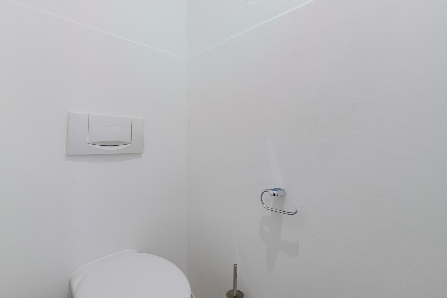 Un baño pequeño y blanco con inodoro, dispensador de toallas de papel y barra para toallas.