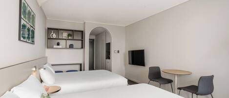 A modern hotel room with two beds, a small table, two chairs, a TV, and a bookshelf.