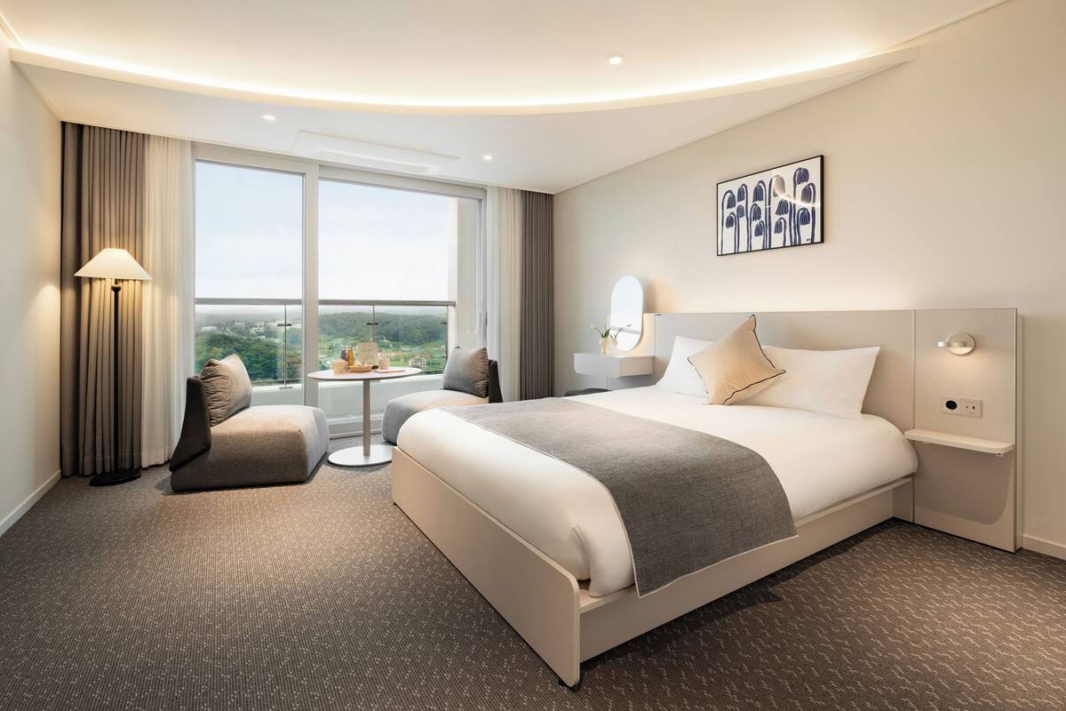 A modern hotel room with a large bed, a seating area, and a view of the city.