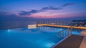 Una piscina con vistas al mar y las luces de la ciudad al atardecer.