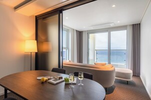A modern hotel room with a dining area, a sofa, and a view of the sea.
