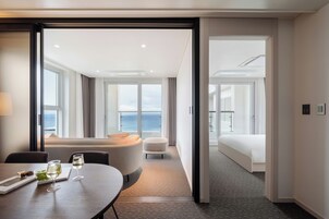 A hotel room with a bed, a seating area with a table, and a view of the ocean.