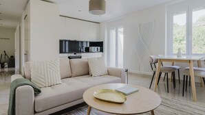 A modern living room with a sofa, a dining table, and a kitchen area with appliances. - Excellent Enge 3BR w/ Balcony, W/D & Elev, by Blueground (Zurich)
