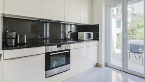 A modern kitchen with a black countertop, stainless steel appliances, and a sliding glass door leading to an outdoor area. - Excellent Enge 3BR w/ Balcony, W/D & Elev, by Blueground (Zurich)