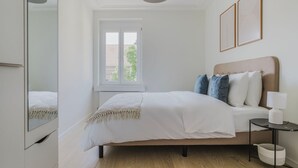 A bedroom with a bed, bedside table, lamp, and a window with a view of buildings. - Excellent Enge 3BR w/ Balcony, W/D & Elev, by Blueground (Zurich)