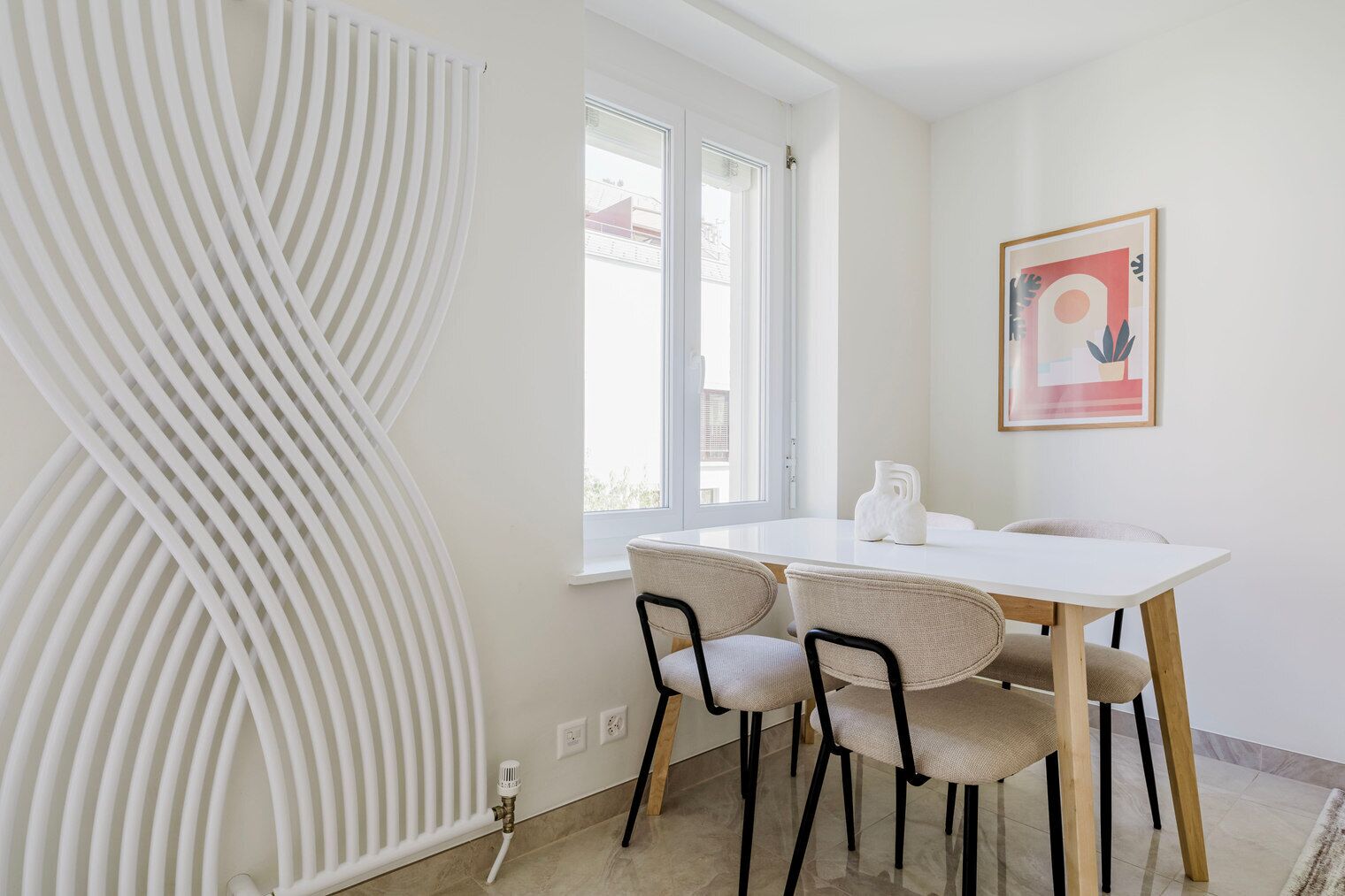 A modern room with a white radiator, a window, a table with chairs, and a framed picture on the wall.