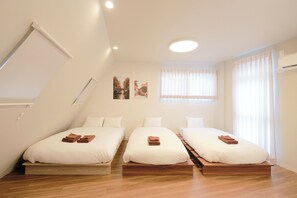Ein Hotelzimmer mit drei Betten, Holzboden und einem großen Fenster mit durchsichtigen Vorhängen.
