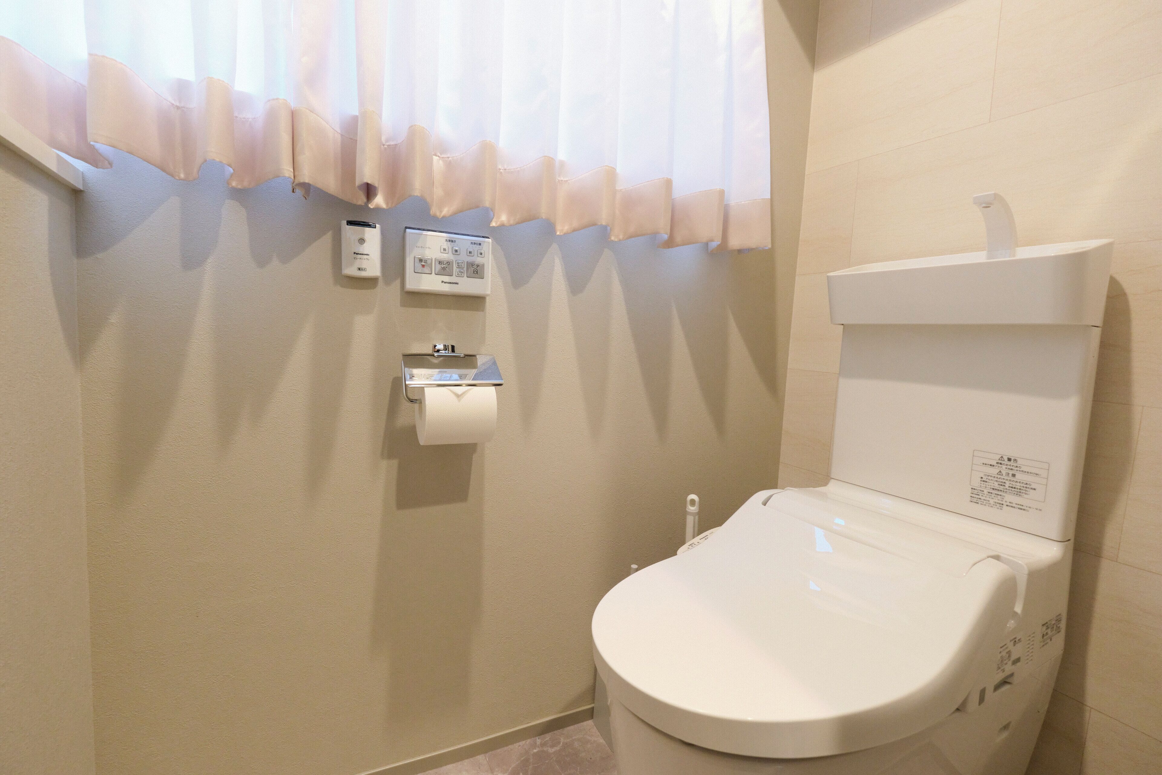 A bathroom with a toilet, a paper towel dispenser, and a toilet paper roll mounted on the wall.
