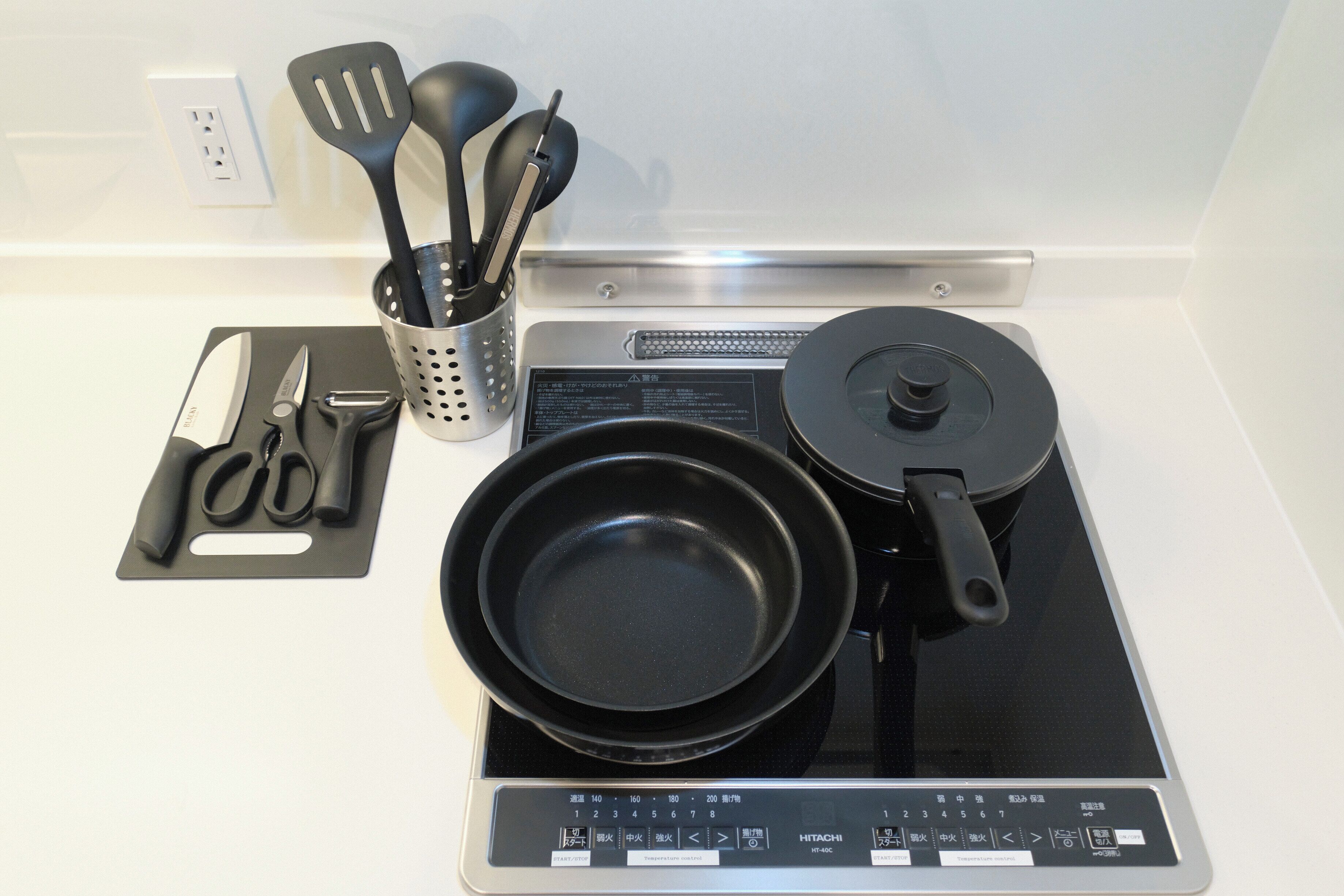 A kitchen with a stovetop, a frying pan, a spatula, a knife, and a pair of scissors.