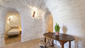 Ein rustikaler Raum mit einem Bett, einem runden Holztisch mit Hockern und einem Blumentopf.