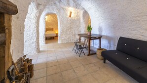 Ein gemütliches Interieur mit einer Steinwand, einem Holztisch mit Stühlen, einem schwarzen Sofa und einem Bett im Hintergrund.