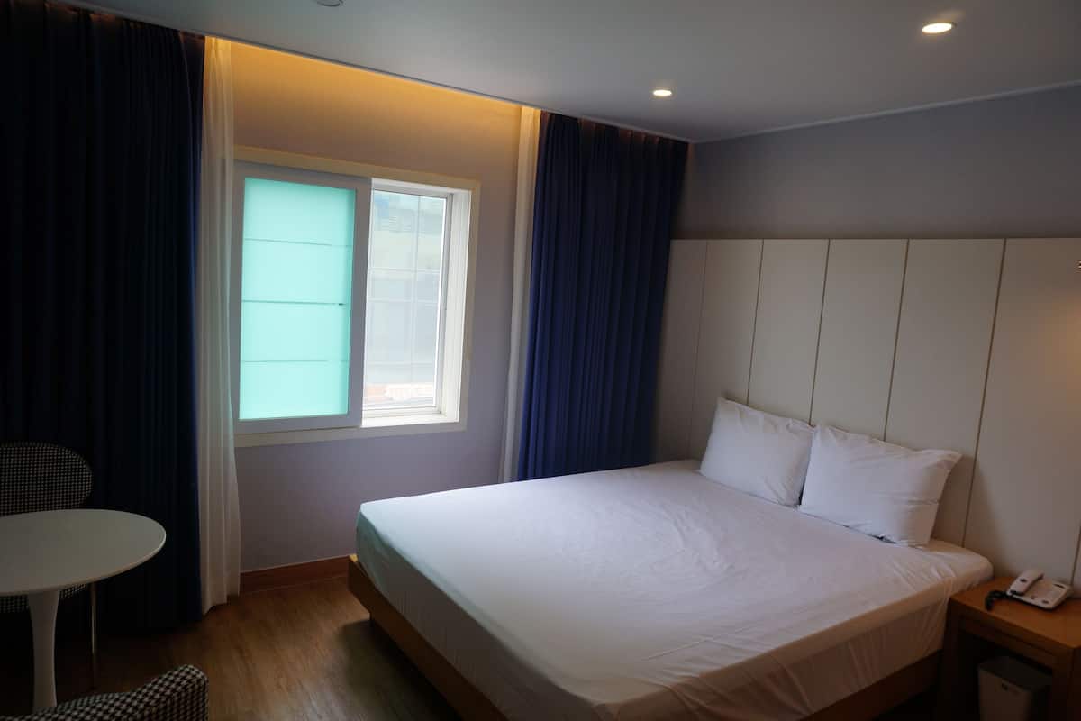 Ein Hotelzimmer mit einem Bett, einem Nachttisch mit Telefon, einem kleinen Tisch und einem Sessel.