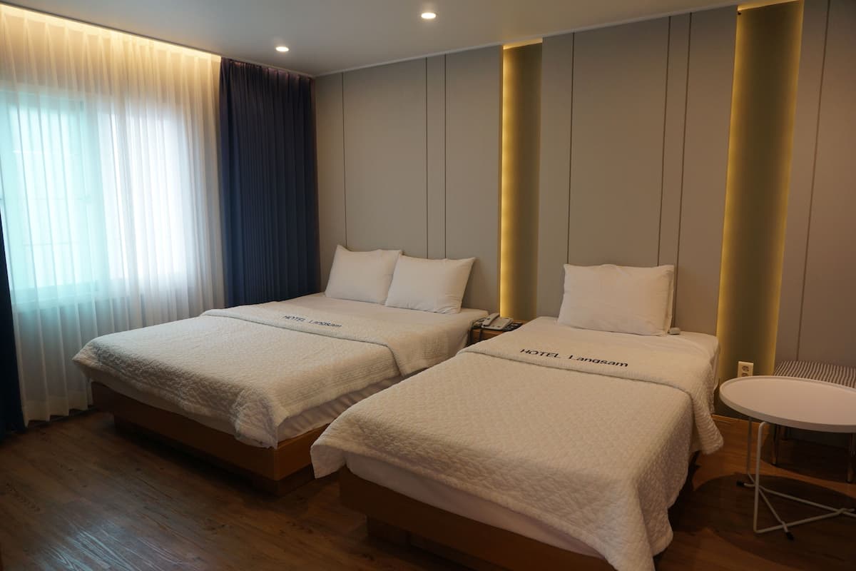 Ein Hotelzimmer mit zwei Betten, einem kleinen runden Tisch und einem Fenster mit Vorhängen.