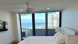 A bedroom with a large bed, a ceiling fan, a TV, and a view of the ocean and buildings. - 2 Bedroom 2 Bathroom Condo on the Beach in Park Shore (Naples)