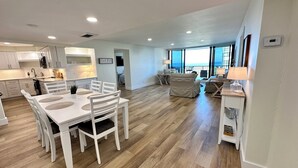 A modern kitchen with white cabinets, a dining area with a white table and chairs, and a living area with a sofa and a lamp. - 2 Bedroom 2 Bathroom Condo on the Beach in Park Shore (Naples)